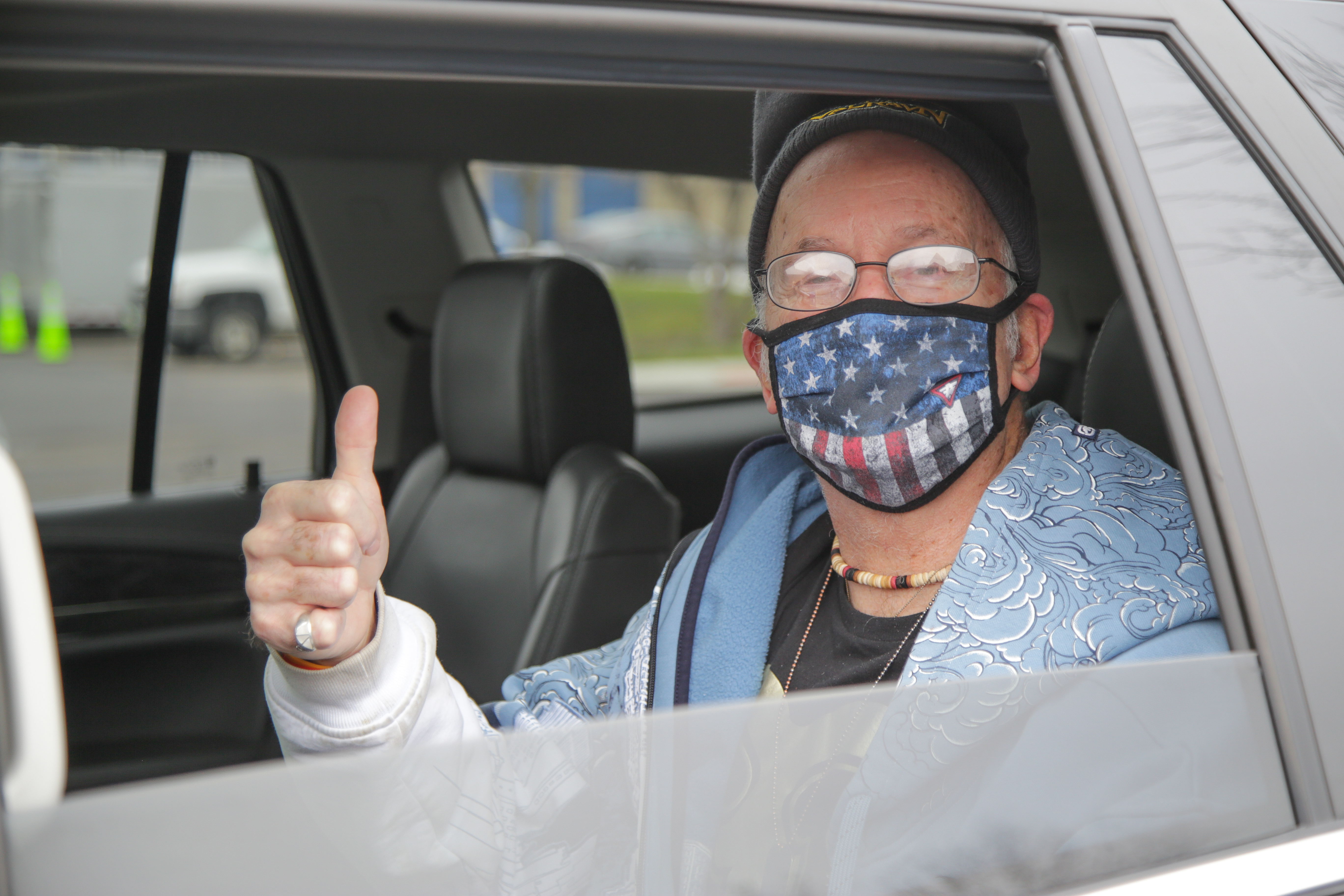 Man with a face covering in a car giving a thumbs up