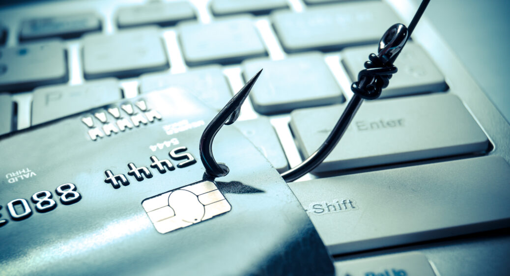 Phishing scam image of fishing hook through a credit card on a computer keyboard