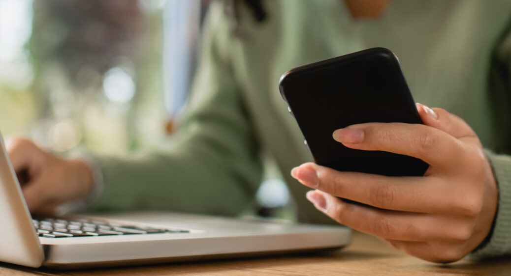 partial view of woman holding phone near laptop on table