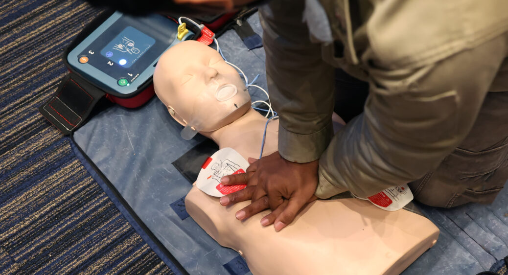 Man practicing CPR on a plastic mannequin with Automated External Defibrillator (AED) on the floor.