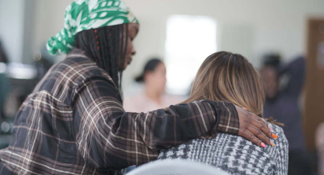 Woman with arm around person in a caring gesture. Both seated with backs to camera angle